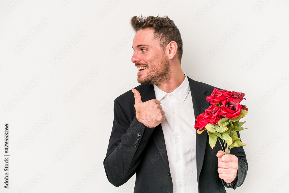 Young caucasian man holding bouquet of flowers isolated on white background points with thumb finger away, laughing and carefree.