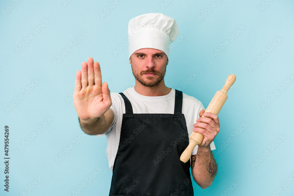 Young baker man isolated on blue background standing with outstretched hand showing stop sign, preventing you. Young baker man isolated on blue background standing with outstretched hand showing stop sign, preventing you.