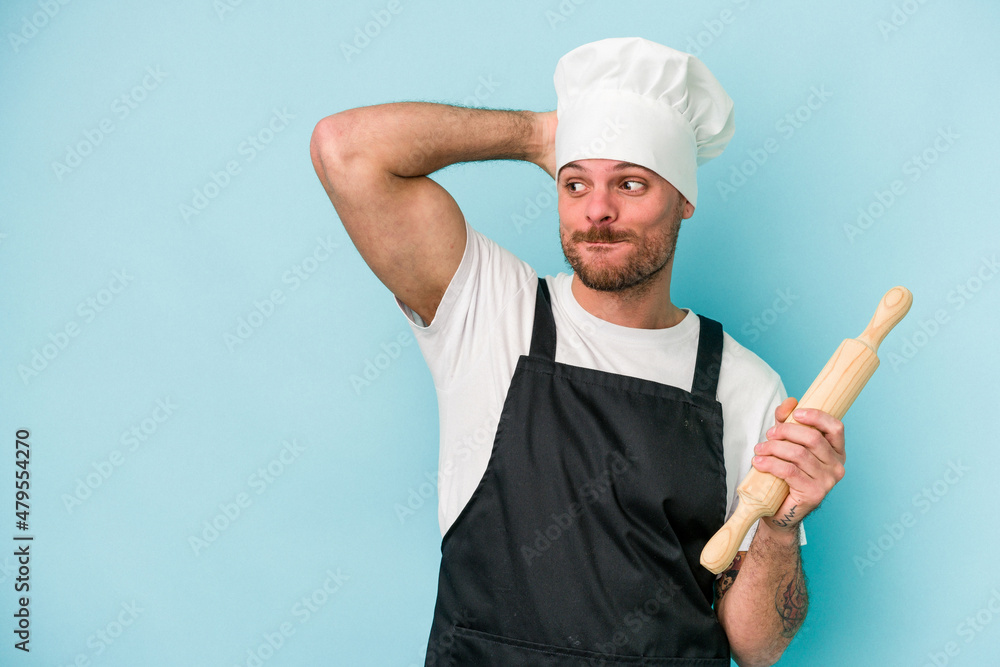 Young baker man isolated on blue background touching back of head, thinking and making a choice. Young baker man isolated on blue background touching back of head, thinking and making a choice.