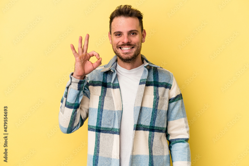 Young caucasian man isolated on yellow background cheerful and confident showing ok gesture. Young caucasian man isolated on yellow background cheerful and confident showing ok gesture.