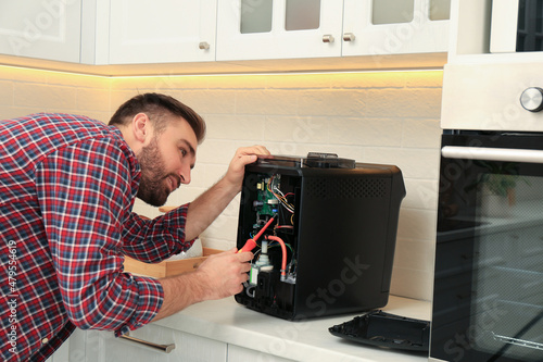 Man with screwdriver fixing coffee machine at table in kitchen