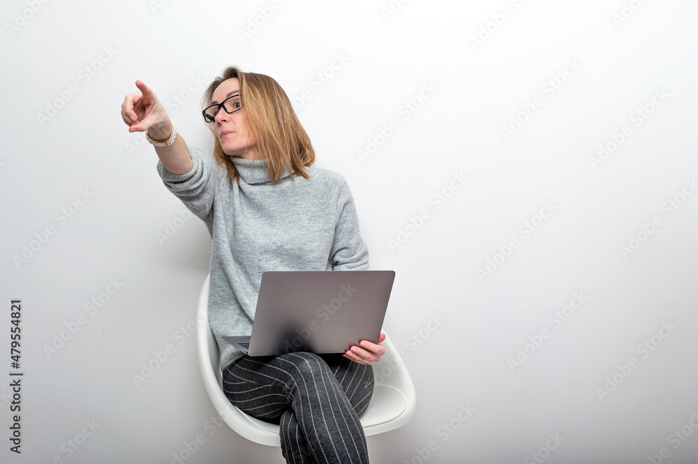 blond woman with glasses and computer pointing finger, isolated on gray blond woman with glasses and computer pointing finger, isolated on gray