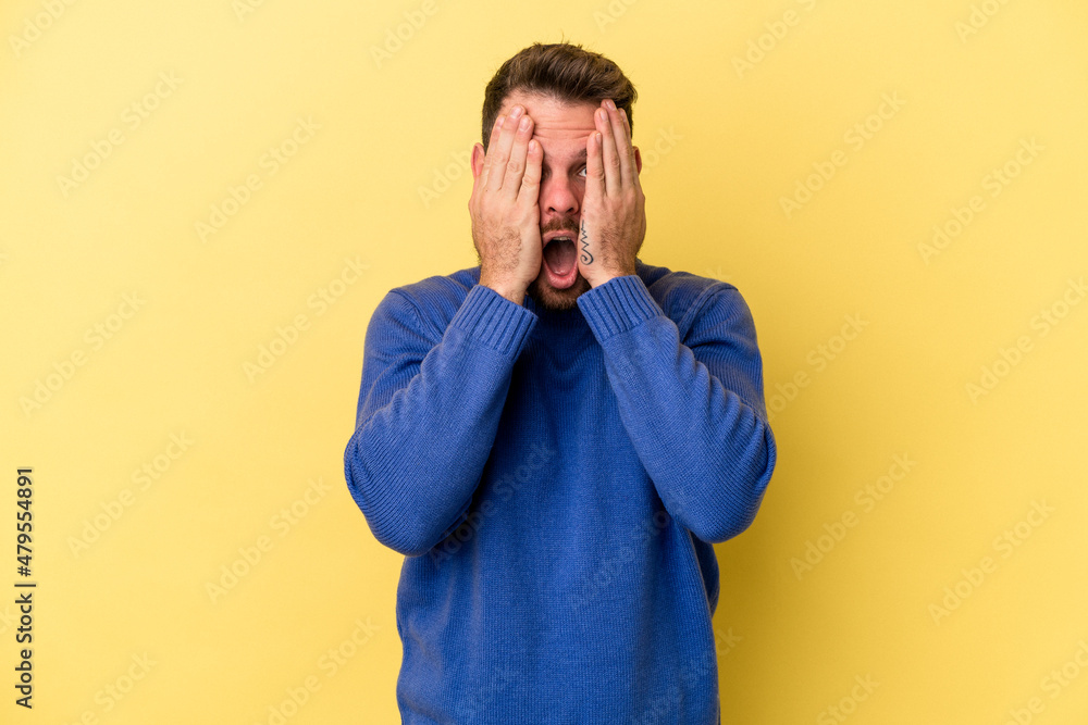 Young caucasian man isolated on yellow background having fun covering half of face with palm. Young caucasian man isolated on yellow background having fun covering half of face with palm.