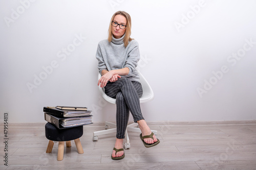 Foto blond woman with laptop on her lap sitting next to a stool with document folders