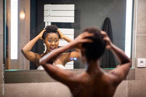 frustrated young black woman adjusting hair in mirror