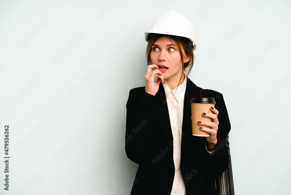 Young architect English woman with helmet and holding blueprints isolated on blue background relaxed thinking about something looking at a copy space. Young architect English woman with helmet and holding blueprints isolated on blue background relaxed thinking about something looking at a copy space.