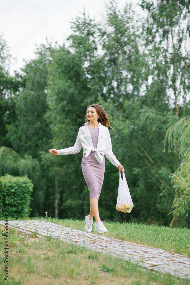 A happy girl runs along a path in the park with an eco-friendly reusable fruit bag. Green life, eco friendly, zero waste concept.