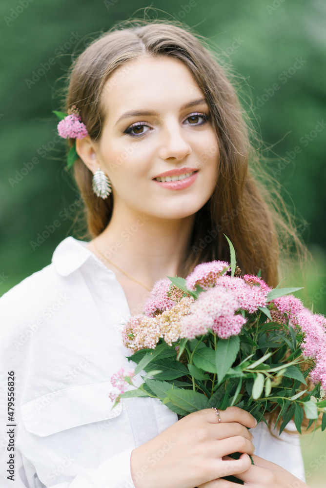 Outdoor close-up portrait of a beautiful young woman with pink flowers on a sunny day in the park. A happy woman received a bouquet of garden flowers from her boyfriend as a gift Outdoor close-up portrait of a beautiful young woman with pink flowers on a sunny day in the park. A happy woman received a bouquet of garden flowers from her boyfriend as a gift