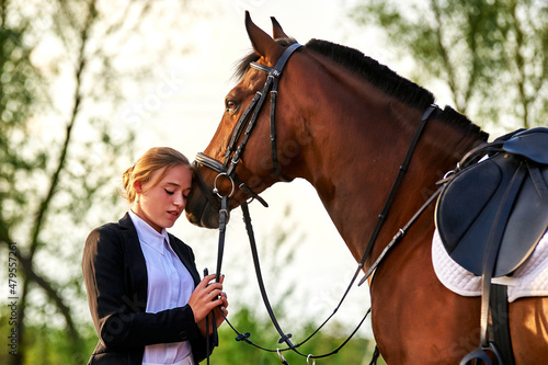 Beautiful horse rider girl stands near a horse on a farm  © Rakursstudio