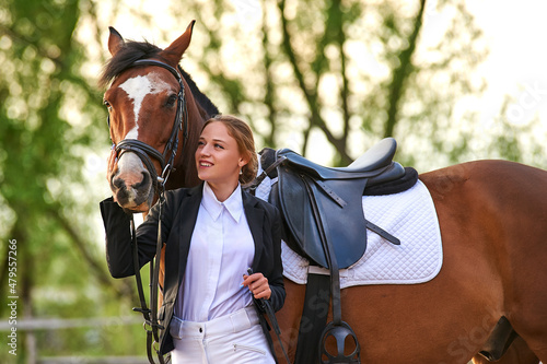 Beautiful horse rider girl stands near a horse on a farm
