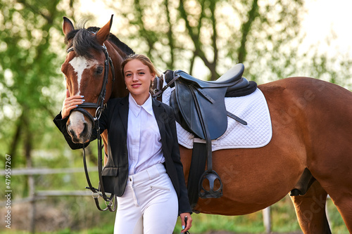 Slika na platnu Beautiful horse rider girl stands near a horse on a farm
