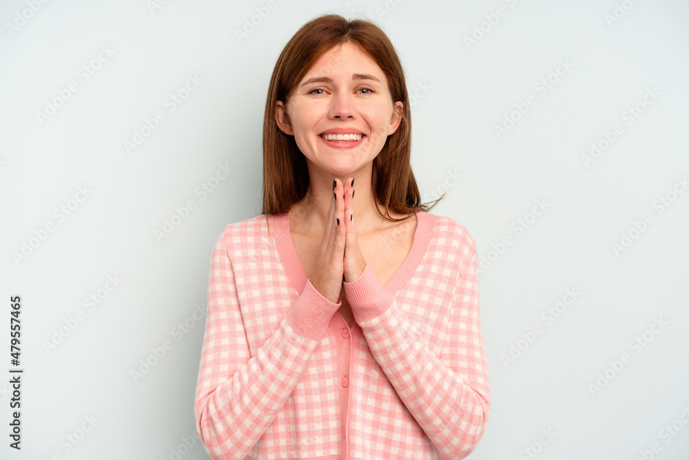Young English woman isolated on blue background holding hands in pray near mouth, feels confident. Young English woman isolated on blue background holding hands in pray near mouth, feels confident.