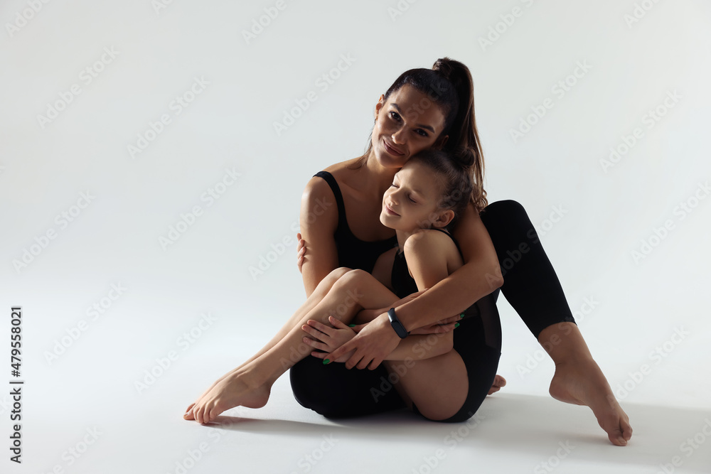 Obraz premium Little gymnast and her coach sitting on white background