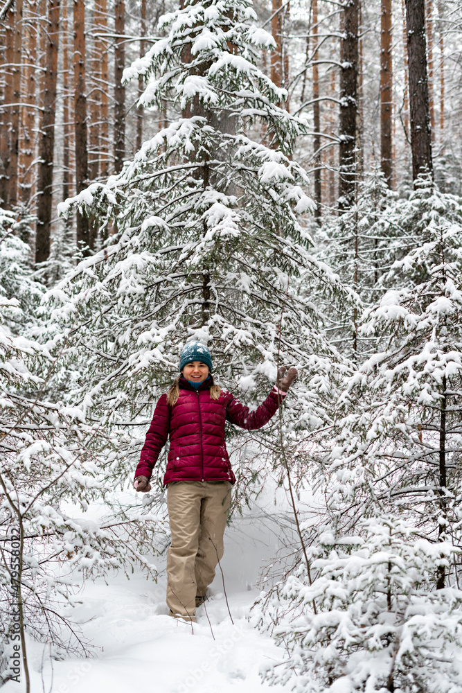 Young cheerful woman in red jacket enjoying snow falling from fir tree in winter forest, walking beauty in nature, active lifestyle winter hiking