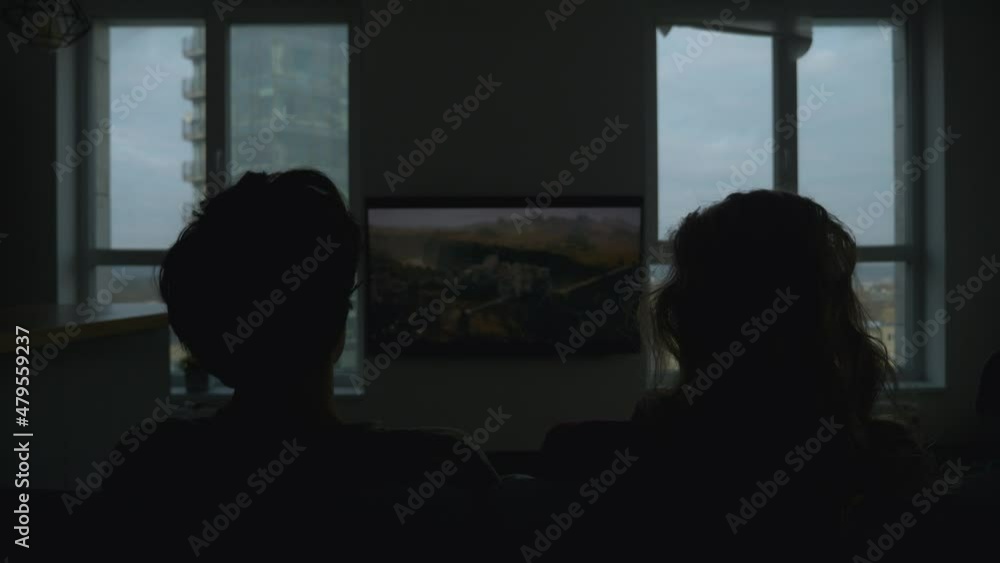 Moving towards camera shot of couple sitting on the couch and watching tv series. Family time. Couple watches new film in the evening. Dark room. Addiction to television. Moving towards camera shot of couple sitting on the couch and watching tv series. Family time. Couple watches new film in the evening. Dark room. Addiction to television.