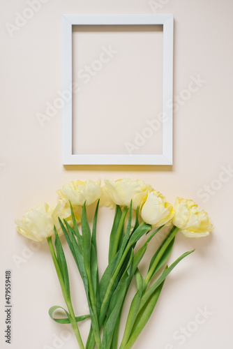 Bouquet of yellow spring tulips on the table  next to an empty white photo frame with copy space. Flat lay