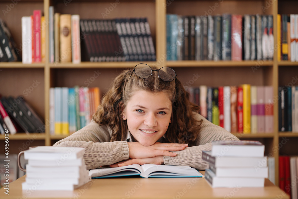Attractive happy young girl student studying at the college library, sitting at the desk Attractive happy young girl student studying at the college library, sitting at the desk