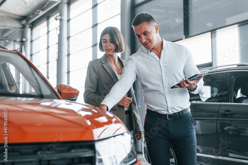 Talking with each other. Man in formal wear helping customer with choice of the automobile