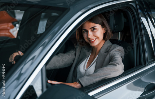 Black colored vehicle. Woman testing new car. Sitting indoors in modern automobile