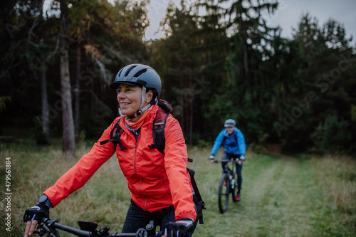 Active senior couple riding bikes outdoors in forest in autumn day.