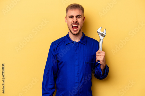 Young electrician caucasian man isolated on yellow background screaming very angry and aggressive.