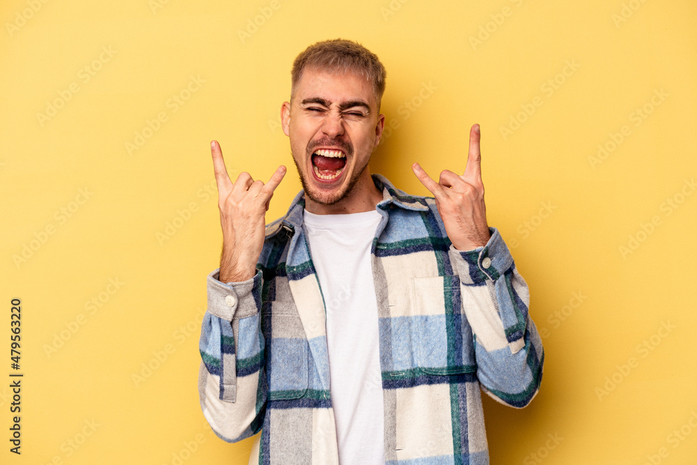 Young caucasian man isolated on yellow background showing a horns gesture as a revolution concept. Young caucasian man isolated on yellow background showing a horns gesture as a revolution concept.