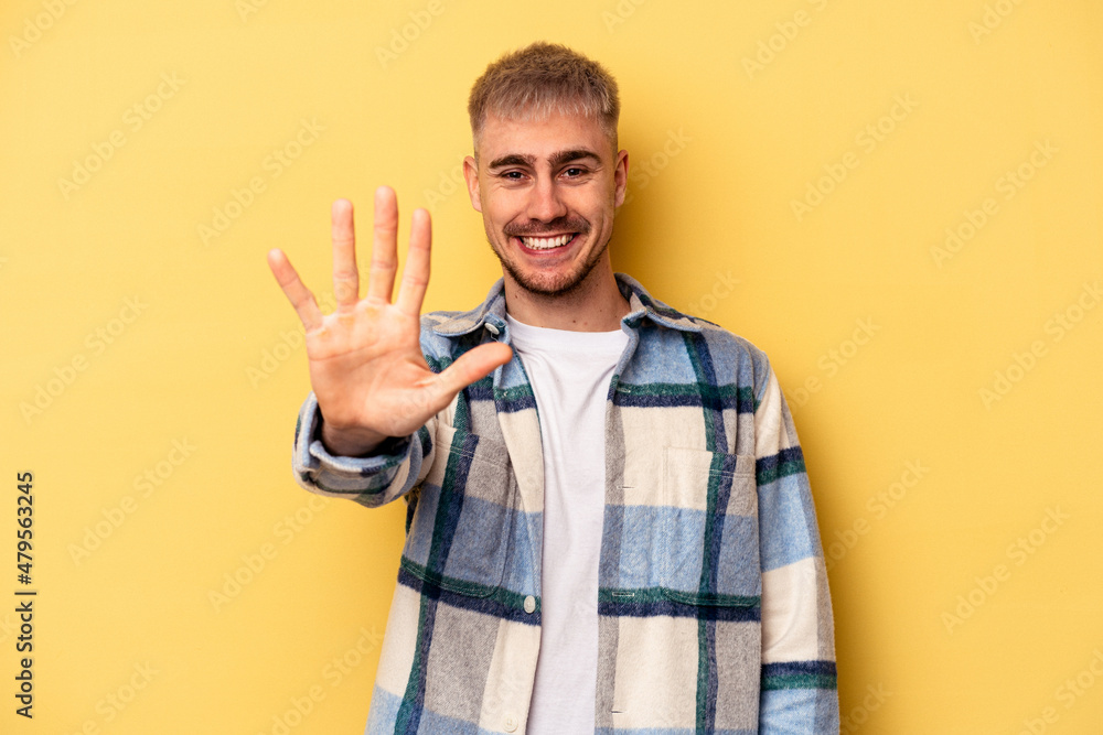 Young caucasian man isolated on yellow background smiling cheerful showing number five with fingers. Young caucasian man isolated on yellow background smiling cheerful showing number five with fingers.