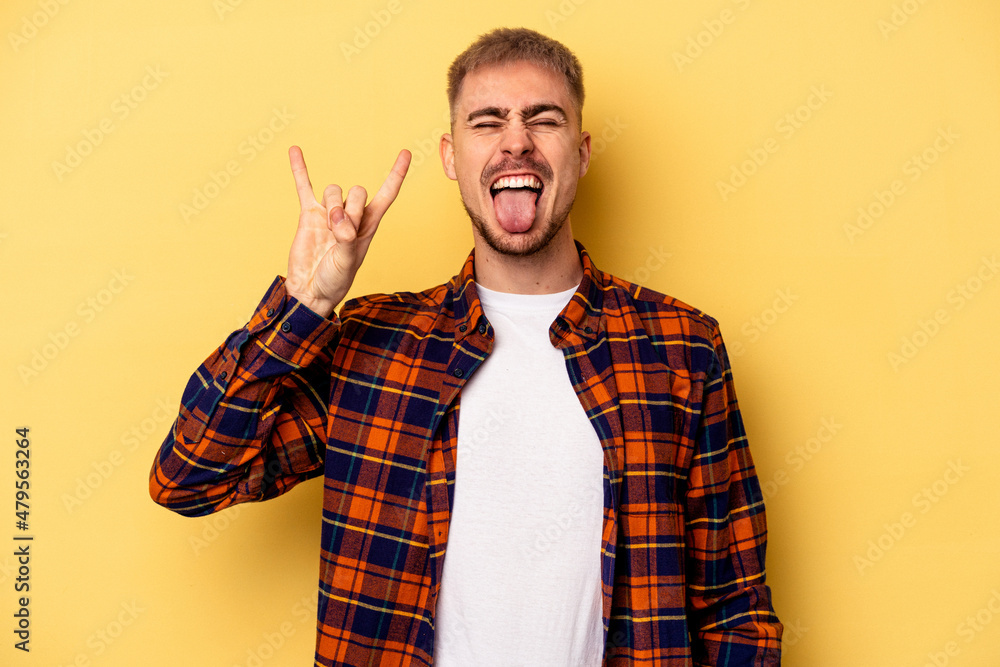 Young caucasian man isolated on yellow background showing rock gesture with fingers Young caucasian man isolated on yellow background showing rock gesture with fingers