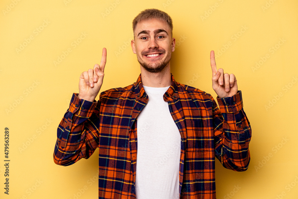 Naklejka premium Young caucasian man isolated on yellow background indicates with both fore fingers up showing a blank space.