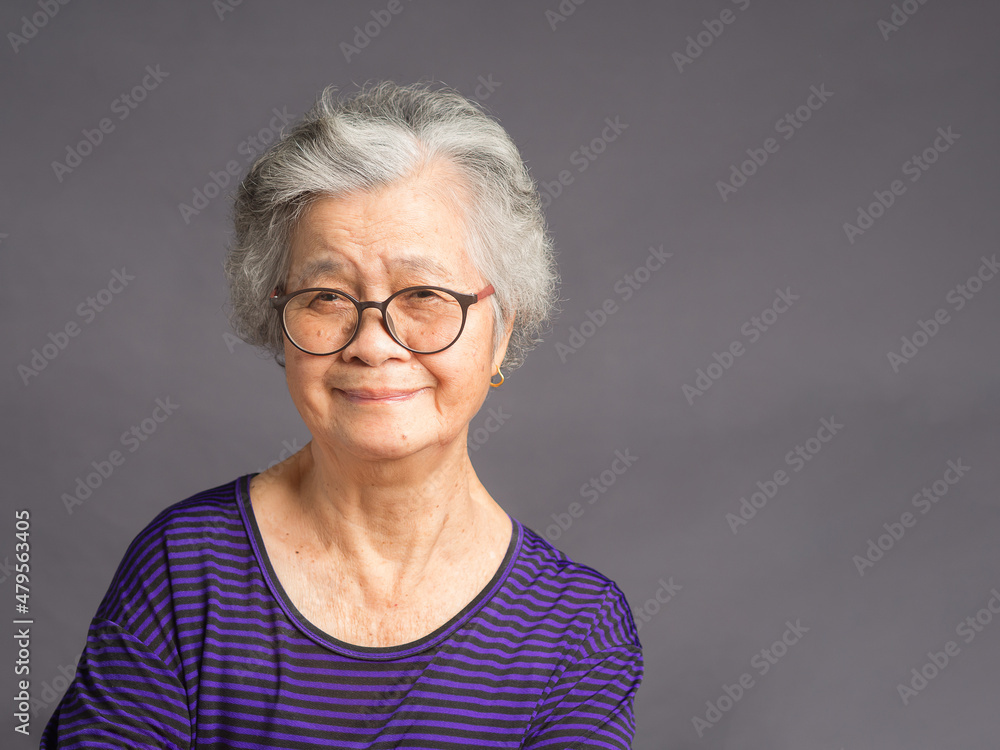 An elderly Asian woman looking at the camera with a smile while standing over a gray background An elderly Asian woman looking at the camera with a smile while standing over a gray background