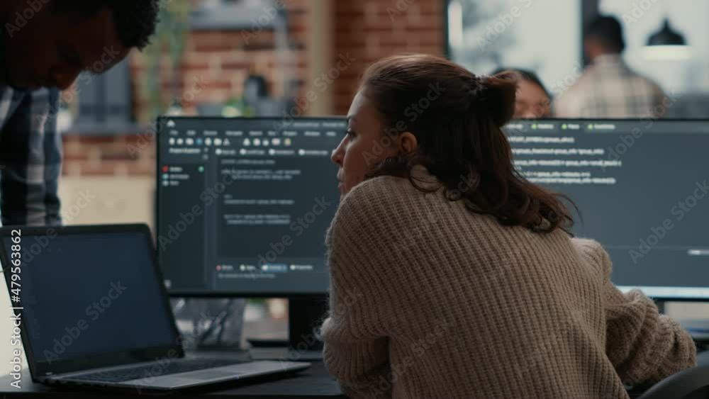 Software programer putting laptop with source code on colleague coder desk asking for opinion about database. Developer writing algorithm interrupted by coworker wanting help with fixing errors.