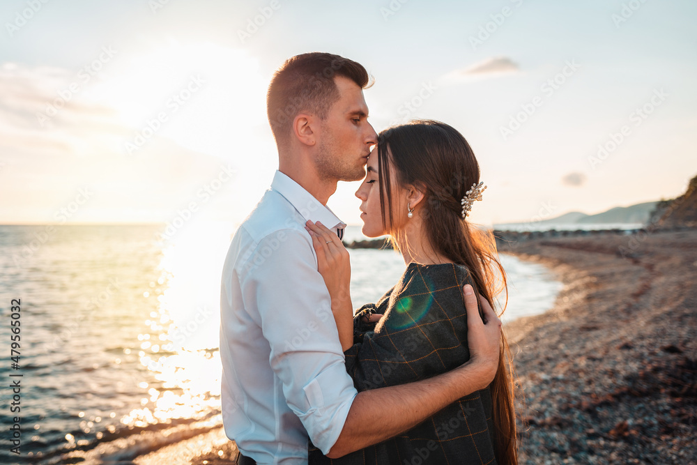 Love and kiss. Husband kisses and hugs his wife. In the background, the ocean and the sunset. Just married concept