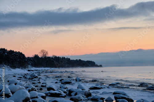 deep snow over rocks at the beach in cold winter sunset by the sea with pine trees and spruce