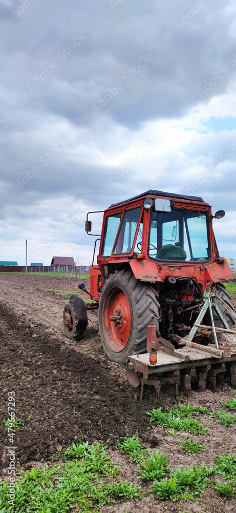 Fototapeta premium Farmer in tractor preparing land with seedbed cultivator as part of pre seeding activities in early spring season of agricultural works at farmlands, vertical view.