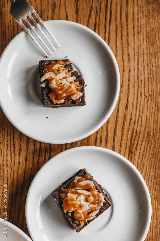 Two brownies on white plates on a wooden table shot from above. Two brownies on white plates on a wooden table shot from above.