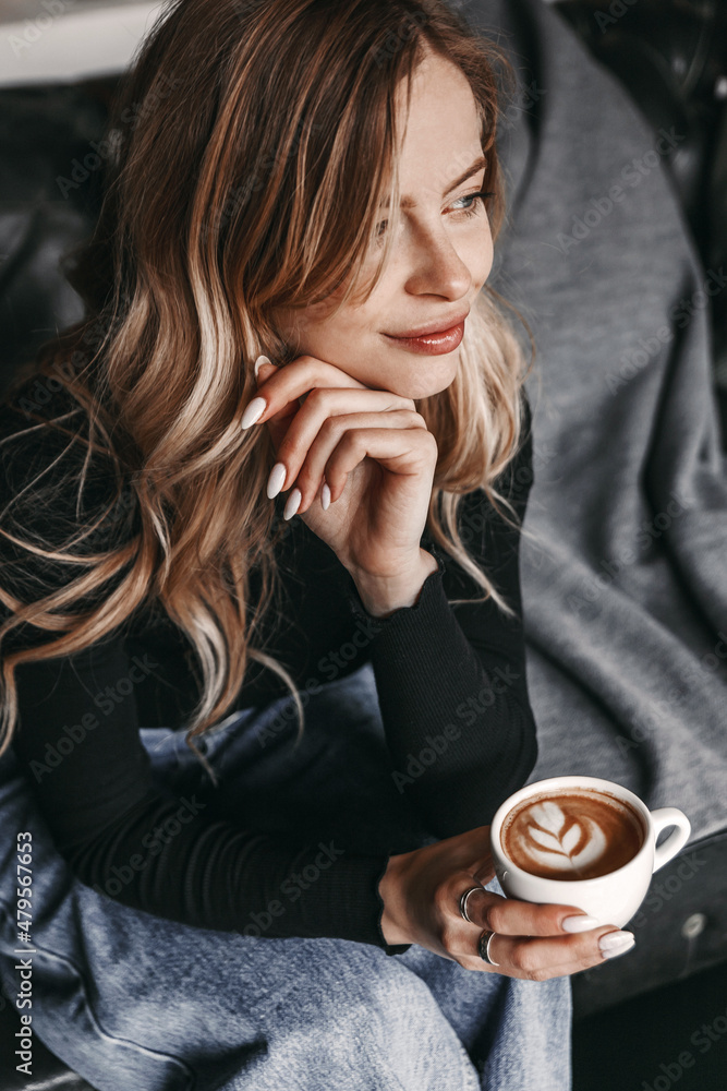 Woman is looking away and she is sitting on a sofa and holding a cup of coffee. Woman is looking away and she is sitting on a sofa and holding a cup of coffee.