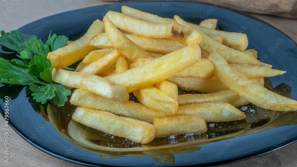 French fries on black dish on parchment background. Tasty golden french fries on a plate. French fries on black dish on parchment background. Tasty golden french fries on a plate.