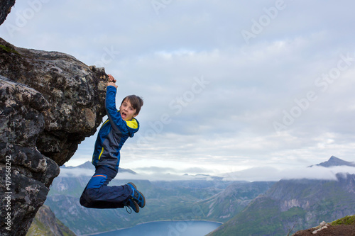 Happy child, hanging from a rock over Segla mountain on Senja island, North Norway. Amazing beautiful landscape and splendid nature