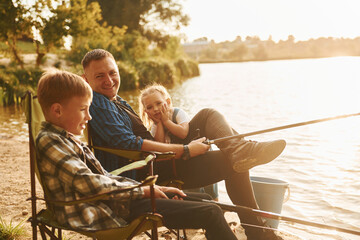 Sitting together. Father with son and daughter on fishing outdoors at summertime