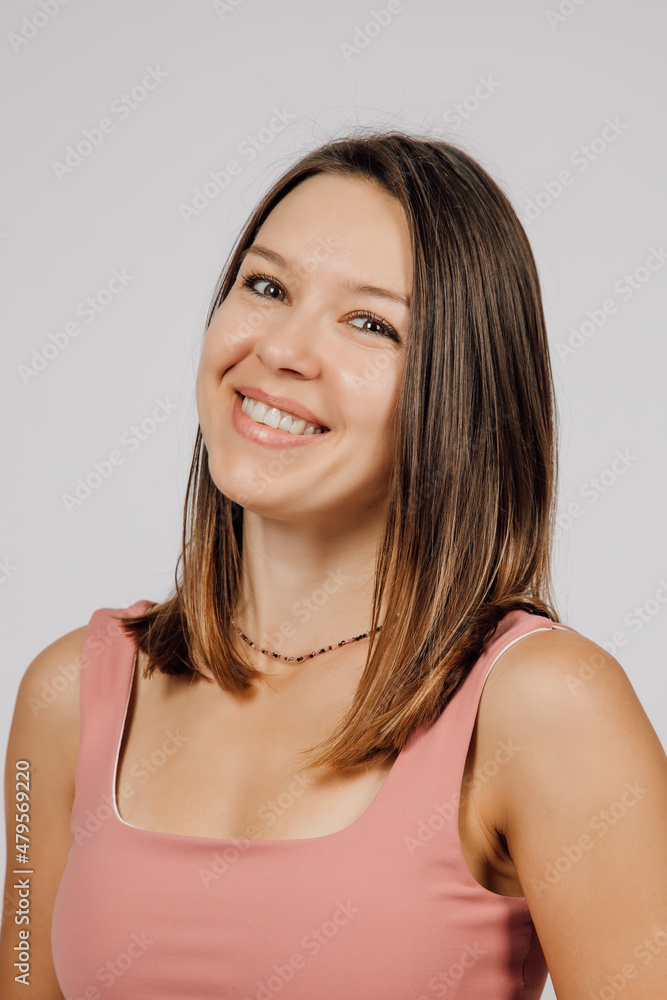 Portrait of smiling brunette. Beautiful happy young woman posing on gray isolated background in studio, she is wearing beige top for yoga or fitness. Portrait of smiling brunette. Beautiful happy young woman posing on gray isolated background in studio, she is wearing beige top for yoga or fitness.