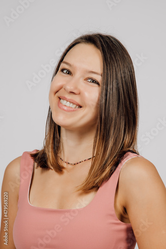 Portrait of smiling brunette. Beautiful happy young woman posing on gray isolated background in studio  she is wearing beige top for yoga or fitness. 