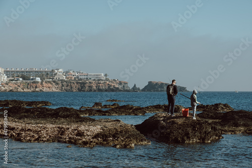 Father and son fishing in a rocky area of ​​Cabo de Palos in Spain on a cloudy winter day