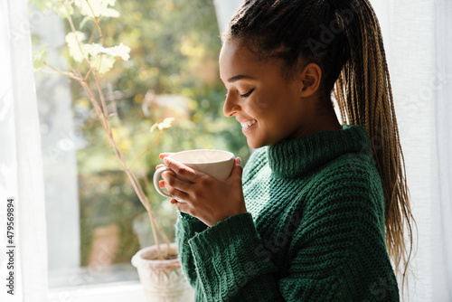 Fotografie, Tablou Young black woman with pigtails smiling while drinking tea