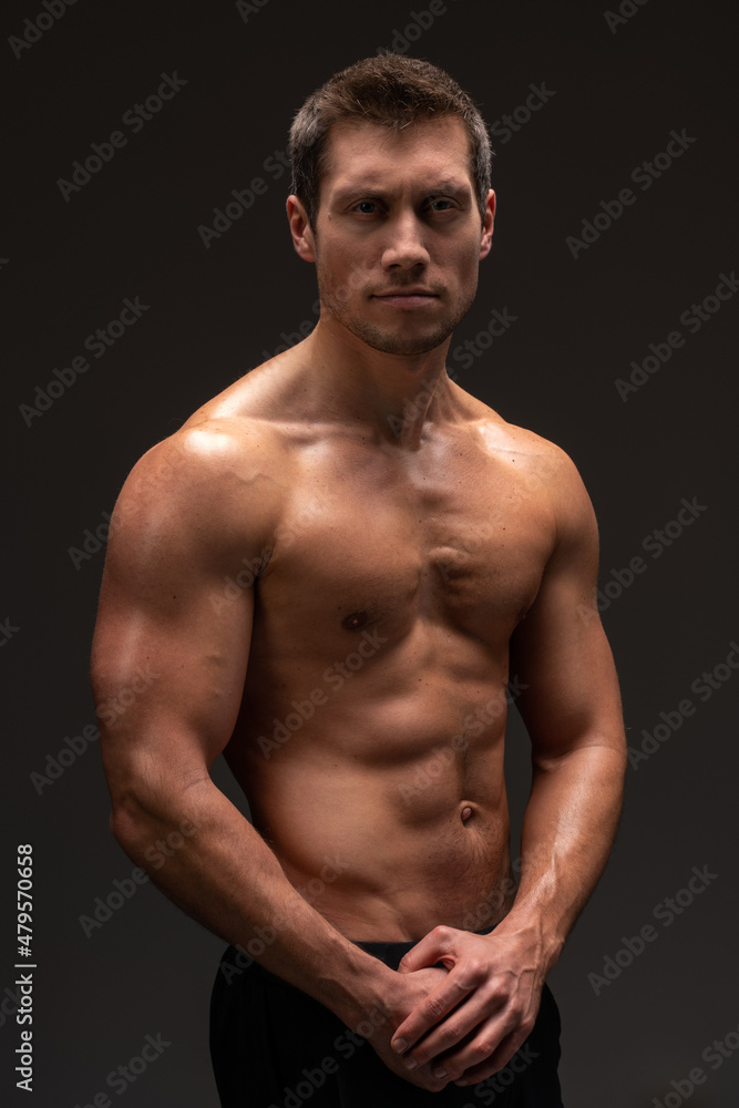 Vertical shot of the handsome muscular guy posing isolated on black background, while showing his strong body and muscles Vertical shot of the handsome muscular guy posing isolated on black background, while showing his strong body and muscles