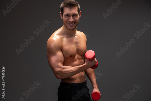 Waist up portrait view of the brunette young man holding red dumbbell over isolated background while making weightlifting