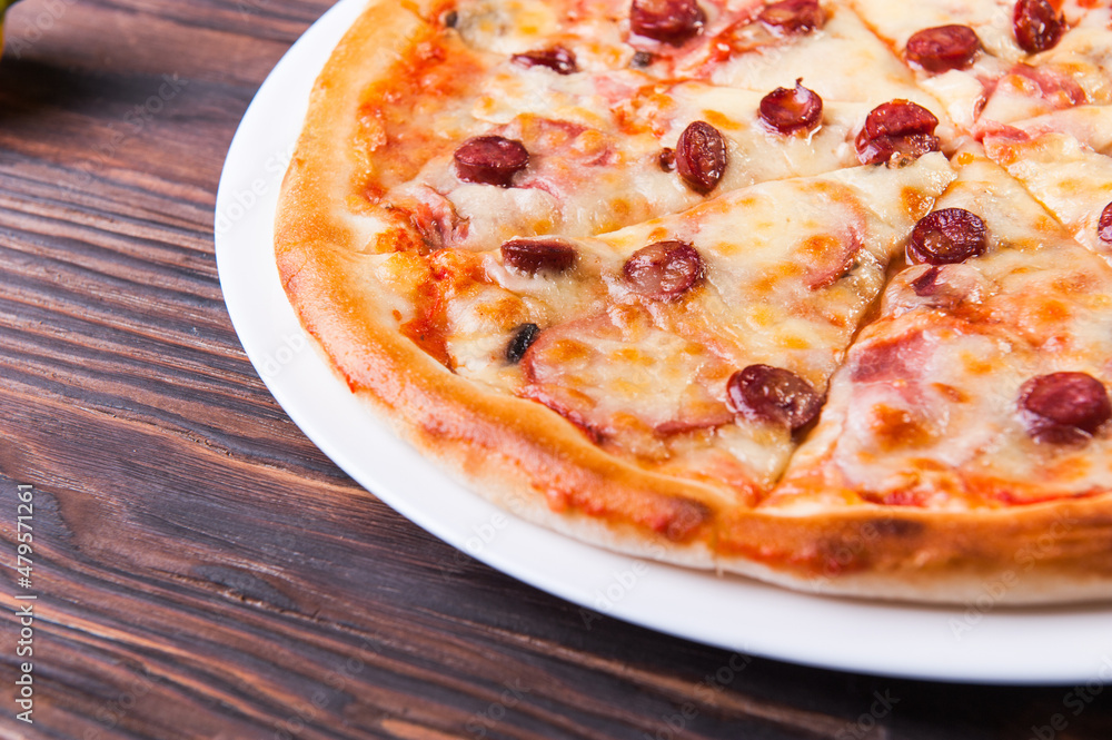 Meat pizza with sausages and cheese lies on a white plate on a wooden table