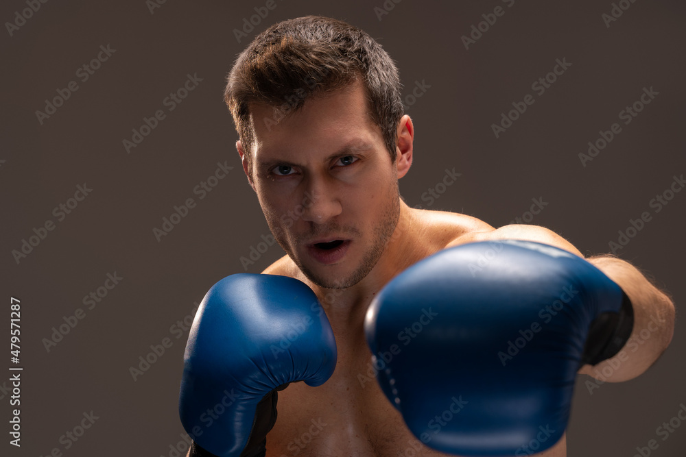 Angry fighter. Aggressive caucasian sports man in boxing gloves looking at the camera over brown background