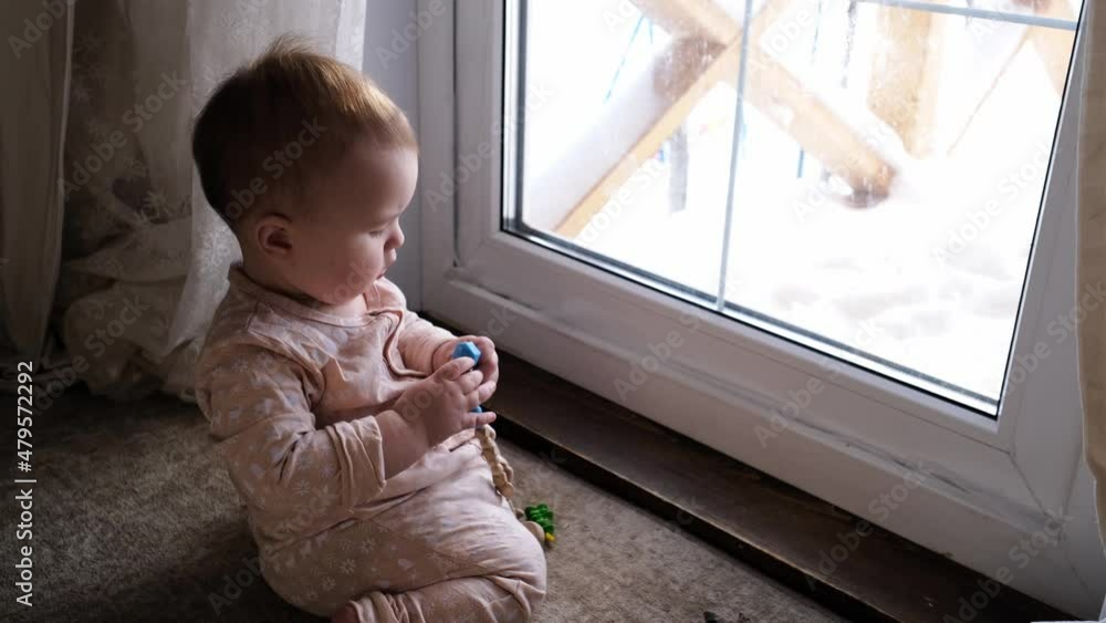A cute plump Caucasian baby 10 months old is gnawing a toy on the floor near the door, window. Safe home space, real interior A cute plump Caucasian baby 10 months old is gnawing a toy on the floor near the door, window. Safe home space, real interior