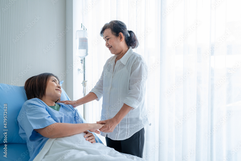 Obraz premium Asian woman, sick, stay in hospital. lying on the patient's bed beside the window Have a mother or an elderly woman come to visit and encourage