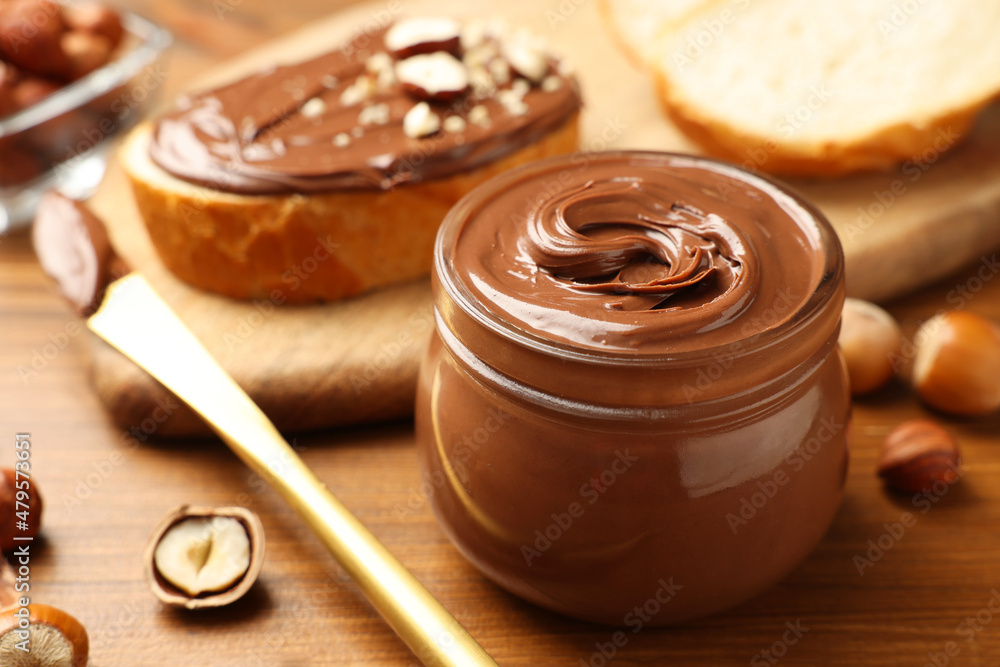 Glass jar with tasty chocolate hazelnut spread and nuts on wooden table, closeup Glass jar with tasty chocolate hazelnut spread and nuts on wooden table, closeup